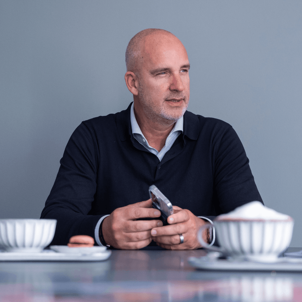 Man met telefoon in zijn hand aan een tafel met koffie